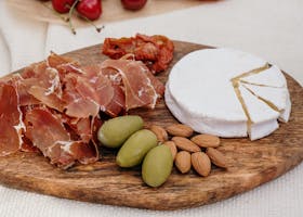 A delectable charcuterie board featuring brie cheese, prosciutto, olives, and almonds.